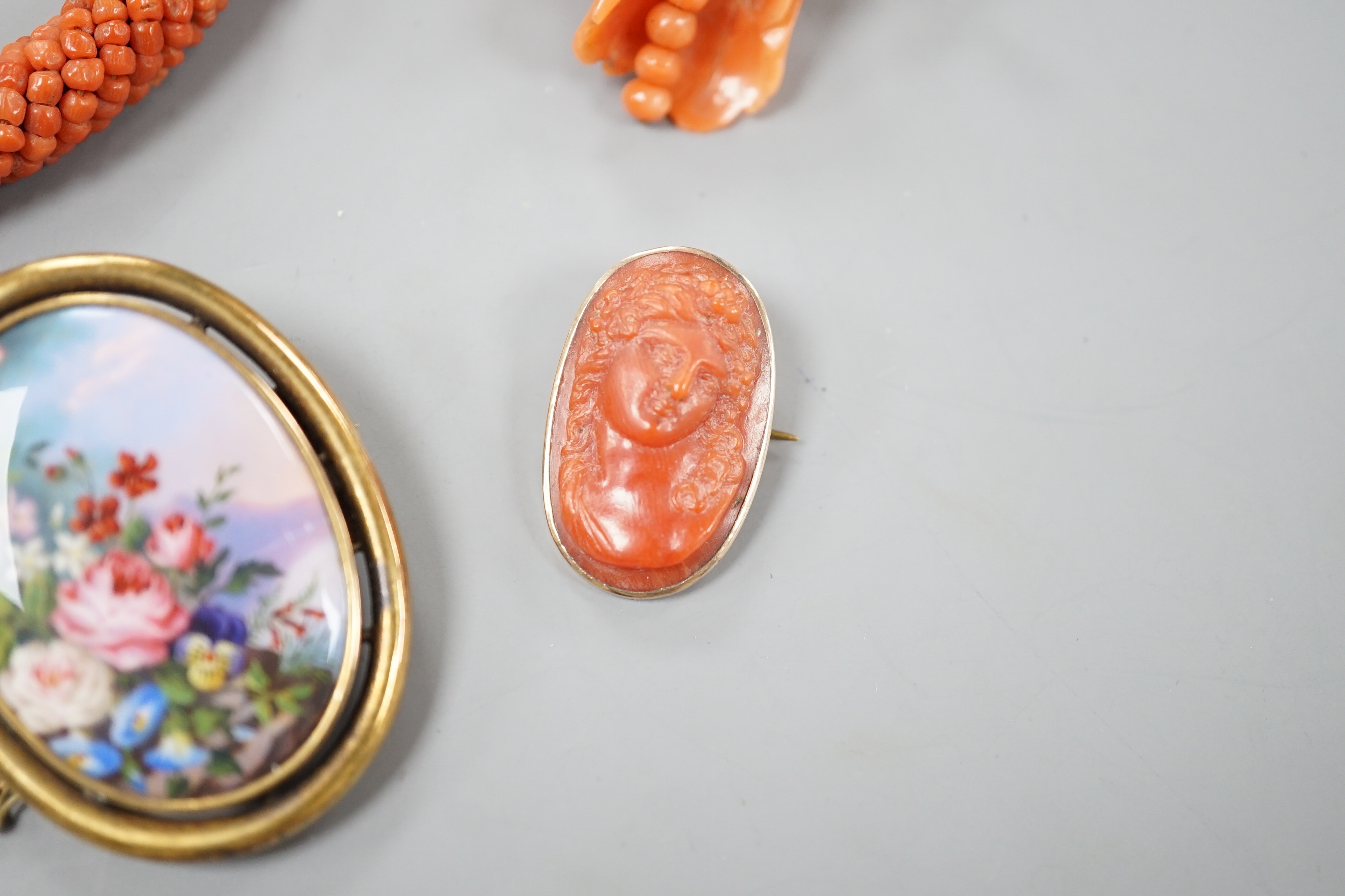 A yellow metal mounted carved coral oval brooch, 30mm, a mounted coral open bangle, a coral brooch and a gilt metal and enamelled brooch.